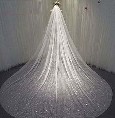 a white wedding veil with flowers on top is hanging in front of a curtained wall