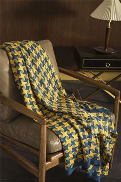 a chair with a yellow and blue blanket on it next to a lamp in a room