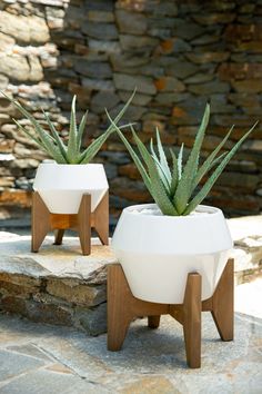 two white planters sitting on top of a stone walkway next to a rock wall