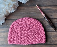 a crocheted pink hat next to white flowers on a wooden surface with a paintbrush