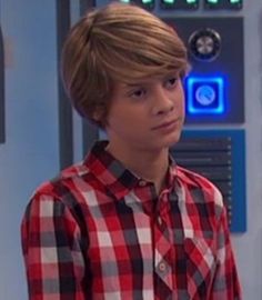 a young boy in a red and black shirt standing next to a locker with buttons on it