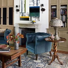 a living room with two blue chairs and a table in front of a fire place