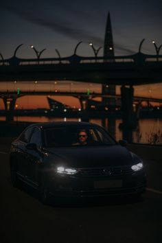 a car driving down the road at night with lights on and bridge in the background