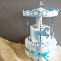 a blue and white carousel cake on top of a cloth covered table with a bow