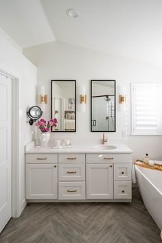 a white bathroom with two mirrors on the wall and a bathtub in the corner