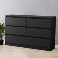 a black dresser sitting on top of a wooden floor next to a potted plant