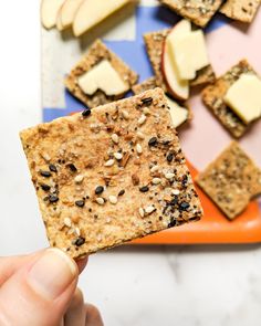 a person holding up a cracker with fruit and cheese on it in front of other snacks