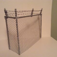 a fence that has some barbed wire on the top and bottom, in front of a white wall