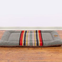 a dog bed on the floor in front of a wall with a striped blanket over it