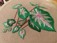 a close up of a embroidery on a piece of cloth with green and pink leaves