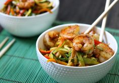 two bowls filled with shrimp and veggies on top of a green place mat