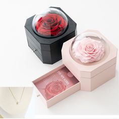 two jewelry boxes with roses in them sitting on top of a white table next to a necklace box