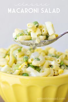 a spoon full of macaroni and cheese with peas on the side in a yellow bowl