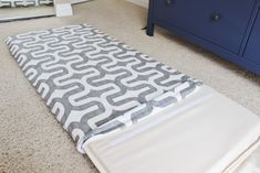 a blue dresser sitting next to a gray and white bed in a room with carpet