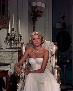 a woman sitting in a chair wearing a white dress and pearls on the neckline