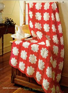 a red and white crocheted blanket sitting on top of a wooden chair next to a table