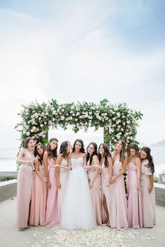 a group of women standing next to each other in front of a flower covered arch