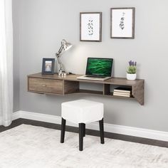 a laptop computer sitting on top of a wooden desk next to a white stool and framed pictures