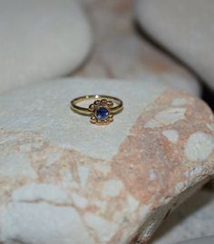 a gold ring with a blue stone in the middle sits on a pile of rocks