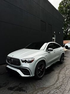 a white mercedes suv is parked in front of a building with black and gray walls