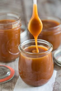 a spoon full of caramel sauce being drizzled over the top of jars