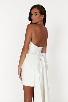 the back of a woman wearing a white dress with a high low cut skirt and heels