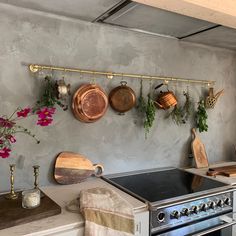 pots and pans hanging on the wall above an oven in a kitchen with flowers