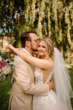 a bride and groom embracing each other in front of a tree with greenery hanging from it