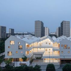 an apartment building with many windows and lights on it's sides in front of some tall buildings