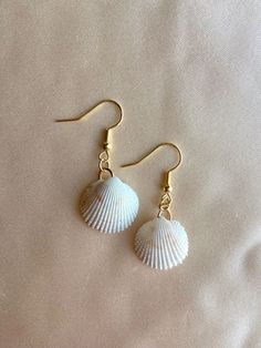 two seashells are hanging from gold earwires on a white sheet,