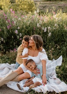 a woman and two children are sitting on a blanket