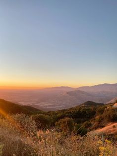 the sun is setting over some hills and trees with mountains in the backround