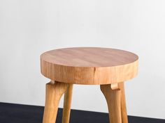 a small wooden stool sitting on top of a black floor next to a white wall