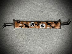 an orange and black beaded bracelet with two cats on it's side, sitting on a gray surface