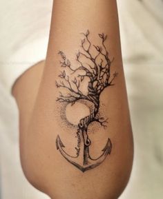 a woman's arm with a tree and an anchor tattoo on the left side