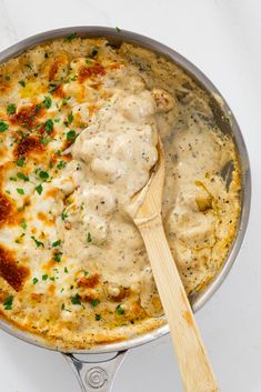 a skillet filled with cheese and sauce on top of a white counter next to a wooden spoon