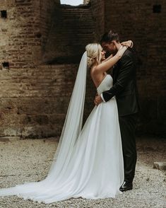 a bride and groom embracing each other in front of an old brick building with stone walls