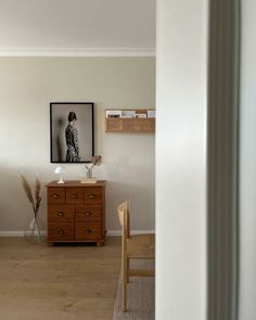 an empty room with a dresser, chair and pictures on the wall in front of it