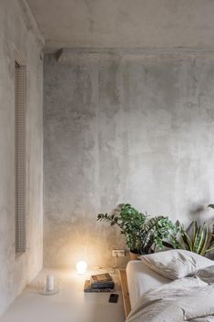 a bed with white sheets and pillows next to a potted plant on a table