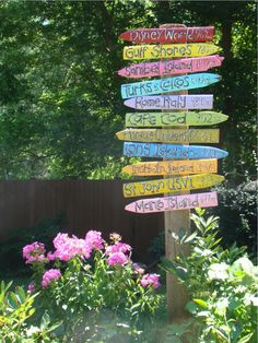 a wooden sign with many different colored signs on it's side in front of some flowers