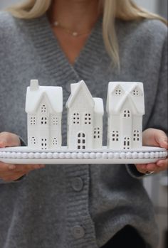 a woman holding three small white houses on a tray