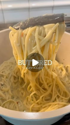 a spoon full of noodles being lifted from a bowl with the word buttered on it