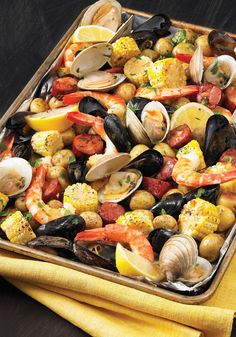 a tray filled with clams, shrimp, corn and mussels on top of a yellow napkin