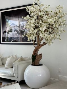 a large white vase with flowers in it sitting on a table next to a couch