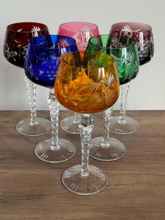 four wine glasses sitting on top of a wooden table with different colored glassware in them