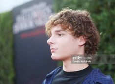 a young man with curly hair wearing a black t - shirt and looking off to the side