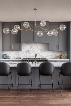 a kitchen with gray cabinets and marble counter tops, along with four chairs in front of the island