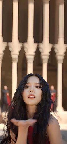 a woman with long black hair standing in front of a white fence and holding her hand out