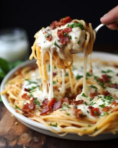 a person is holding a fork full of spaghetti with bacon and cream sauce on it