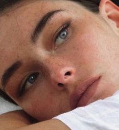 a woman with freckled hair and blue eyes laying on a bed looking at the camera